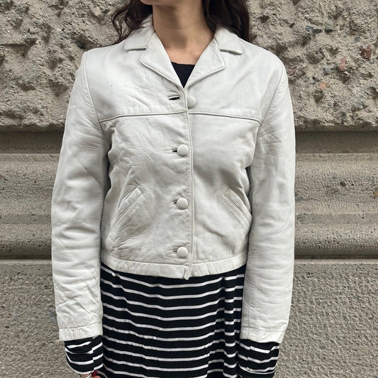 Person wearing a light-colored jacket and black and white striped skirt against a stone wall.