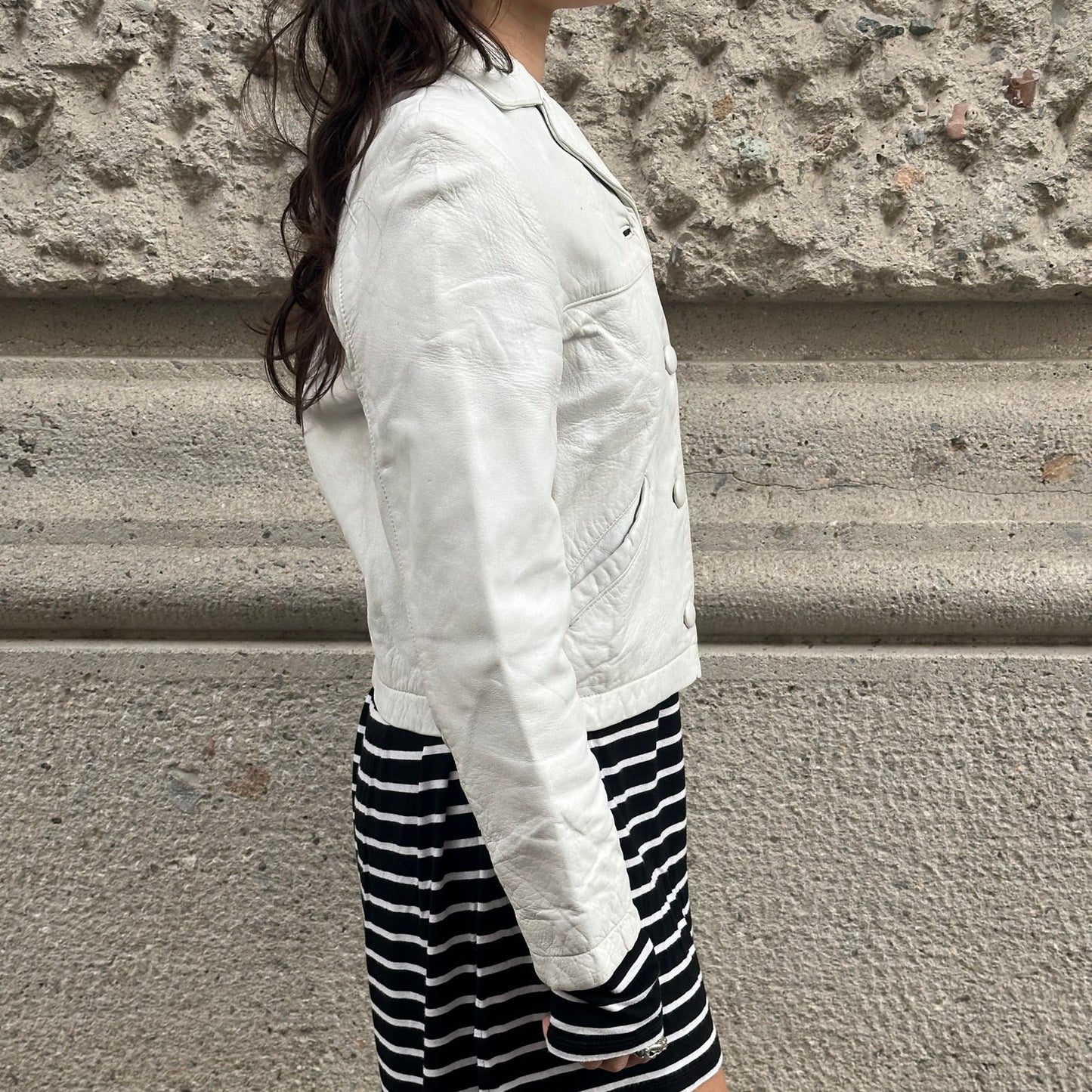 Person wearing a white jacket and black and white striped shorts against a stone wall.