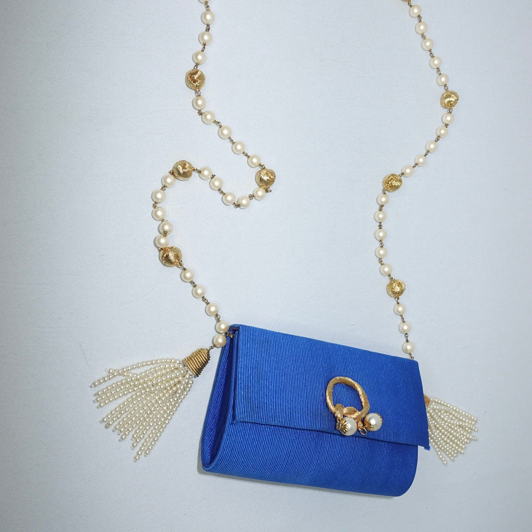 Blue handbag with gold accents and pearl tassels on a light white background