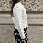 Person wearing a white jacket and black and white striped shorts against a stone wall.