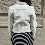 Person wearing a light-colored jacket and black and white striped skirt against a stone wall.