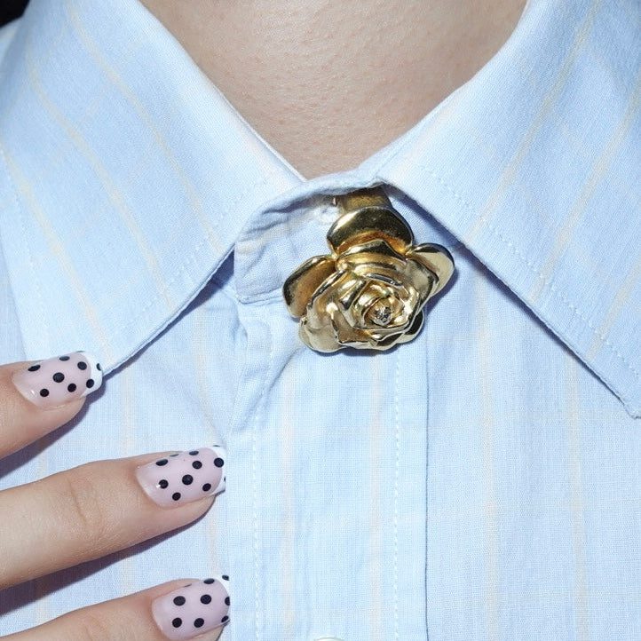 Gold rose brooch on a light blue striped shirt with polka dot nail design.