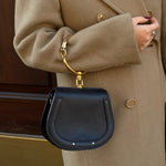 Person wearing a beige coat holding a black handbag with gold accents.