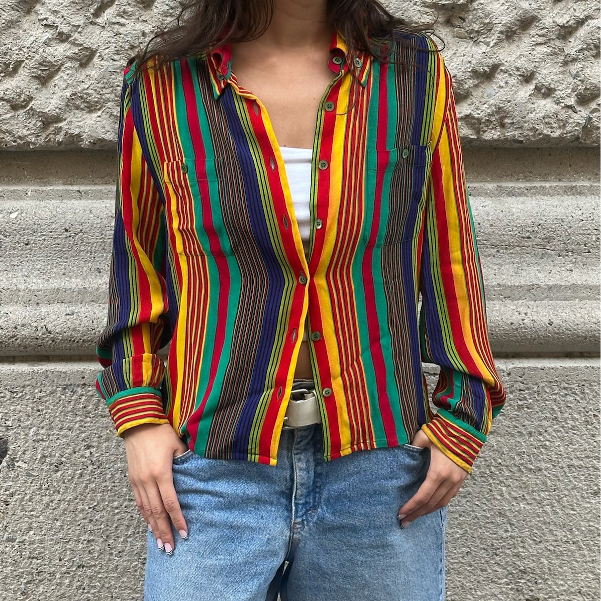 Person wearing a colorful striped shirt against a stone wall.