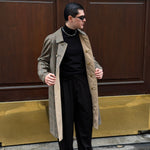Man in a coat standing in front of a door with a gold doorknob.