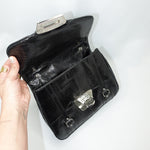Black handbag with silver clasp held by a hand on a white background