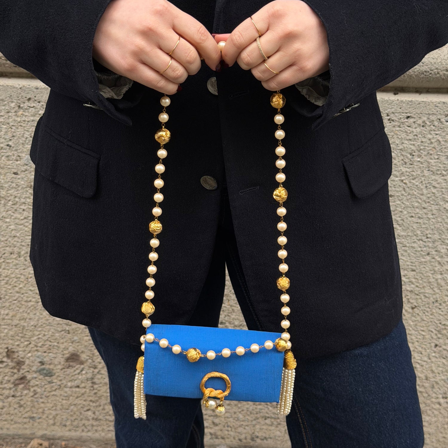 Person holding a blue handbag with pearl strap against a neutral background