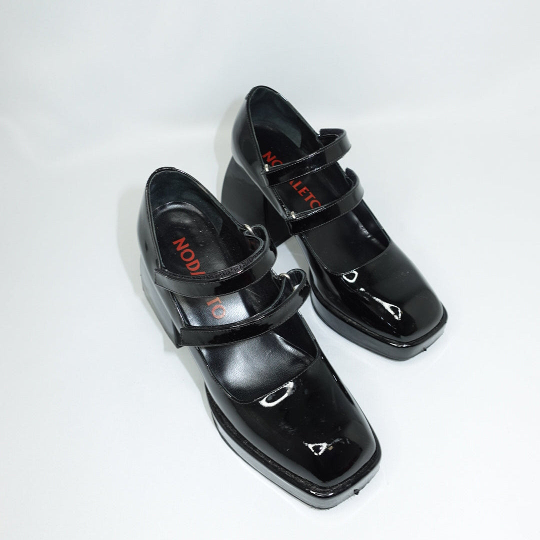 Black patent leather shoes with strap design on a white background