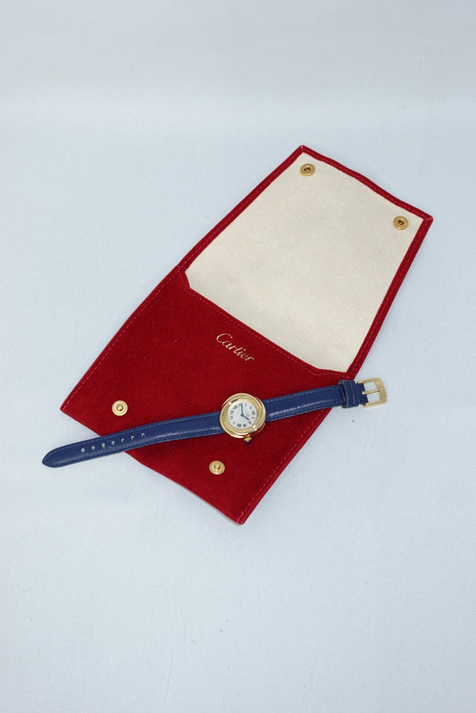 Front view of the Cartier Trinity vintage watch showcasing the classic dial design and the warm gold toned case paired with a refined blue leather strap. A perfect example of Cartier’s timeless aesthetic and elegant proportions. Cartier watch with blue strap on a red cushion against a light gray background