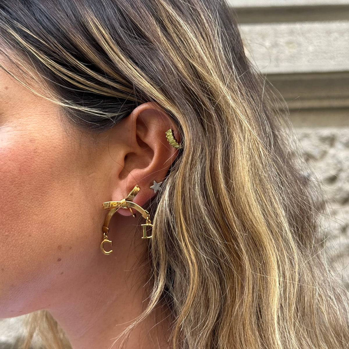 Vintage Christian Dior gold-toned ribbon bow earrings worn by model with dangling Dior letter charms