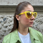 Person wearing yellow sunglasses and a light green jacket on a textured wall background