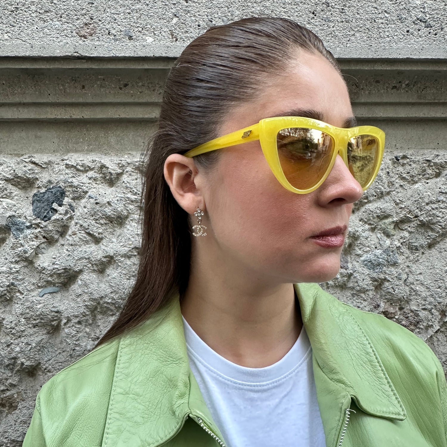 Person wearing yellow sunglasses and a light green jacket on a textured wall background
