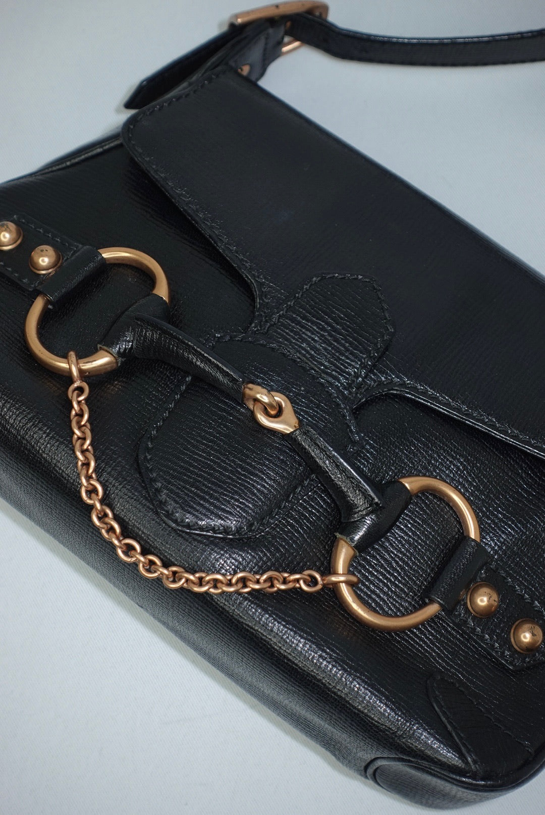 Close-up detail of the iconic Gucci horsebit hardware in a warm bronze tone, showing natural patina and vintage character against the black leather background.