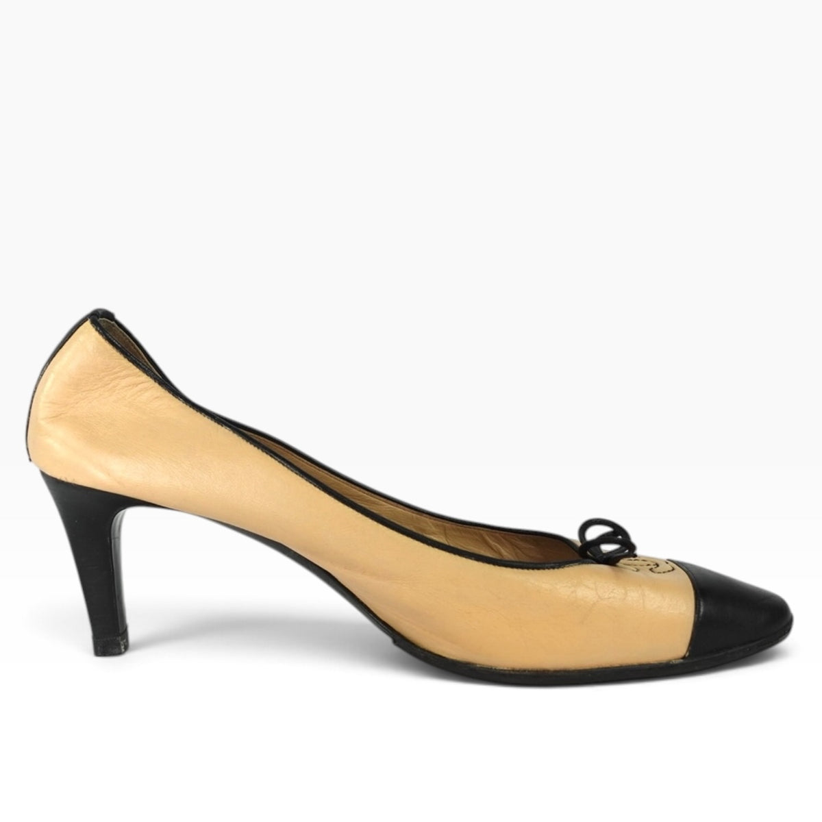 Chanel beige leather pumps with black cap toe, piping, and bow detail featuring the iconic CC logo.