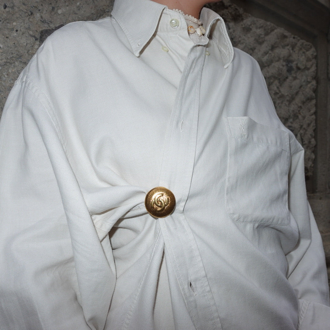 Vintage Chanel gold CC logo brooch worn on a ruched shirt showing statement styling