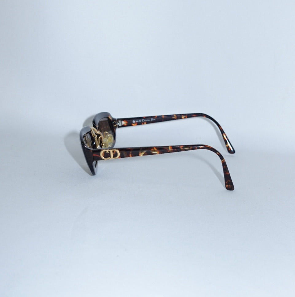 Side profile of Christian Dior tortoiseshell sunglasses showcasing the signature gold CD logo on the temple.
