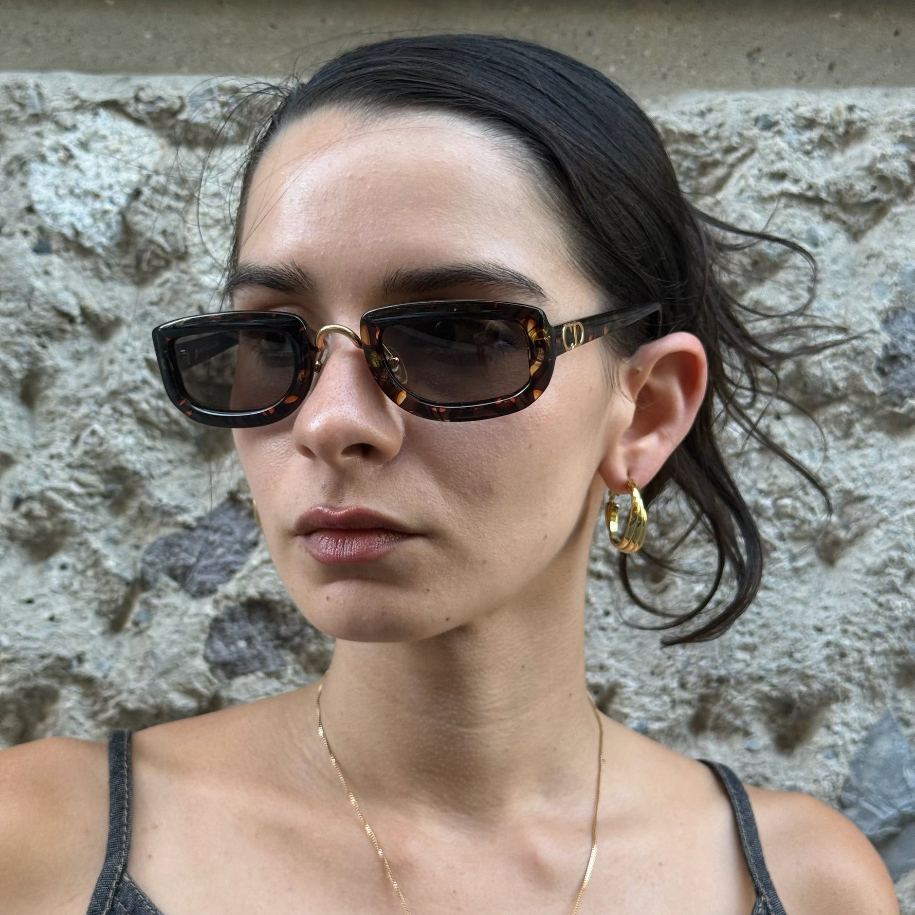 Model wearing Christian Dior tortoiseshell rectangular sunglasses with brown tinted lenses and iconic gold CD logo detail.