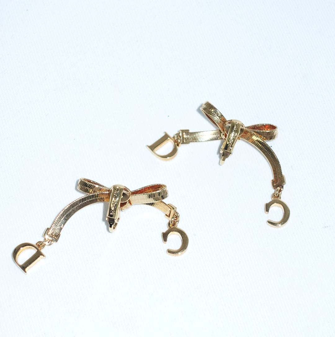 Vintage Christian Dior gold-toned ribbon bow earrings still life with dangling Dior letter charms