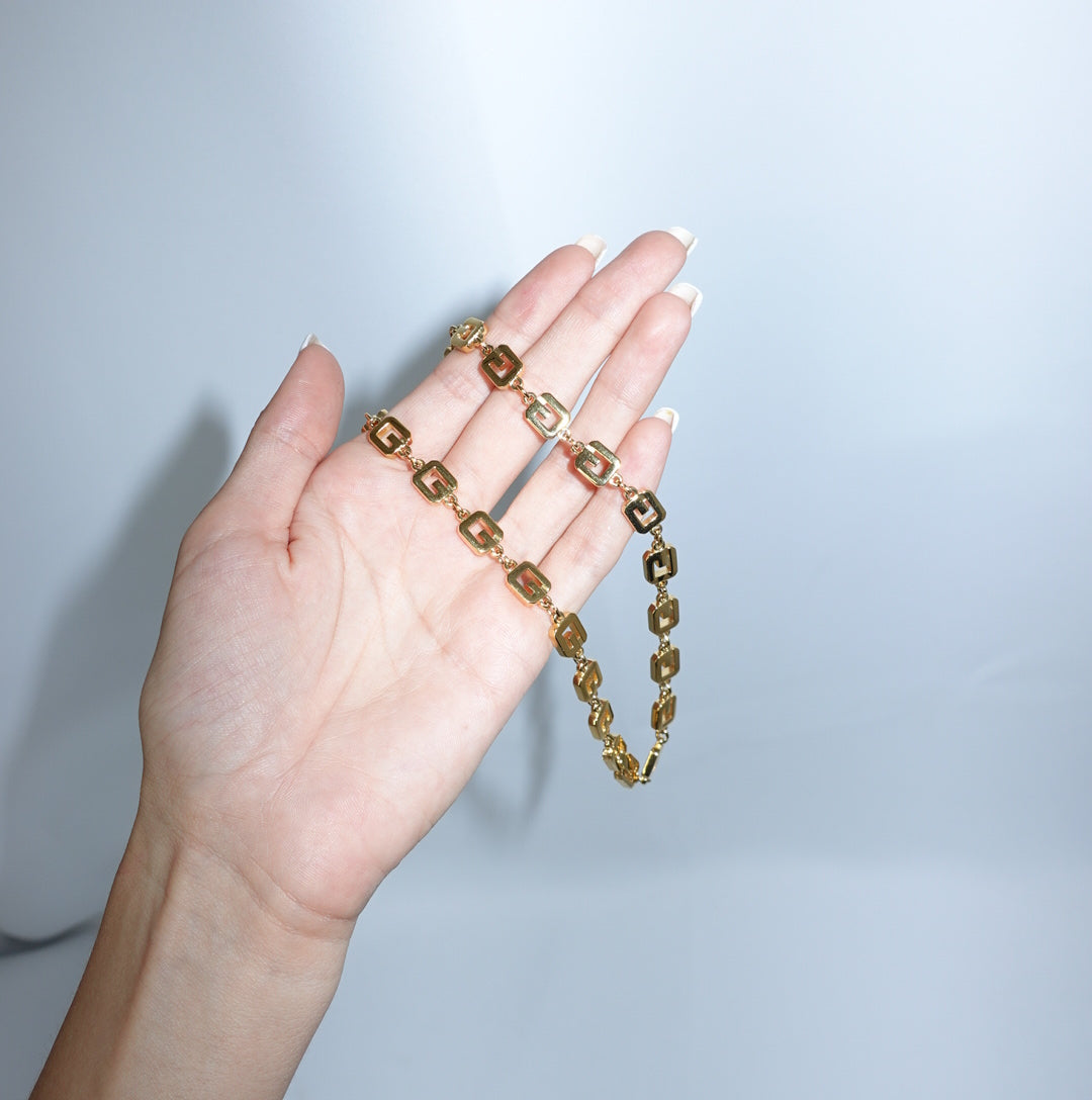 Vintage Givenchy gold-toned logo link necklace held close-up showing geometric chain details