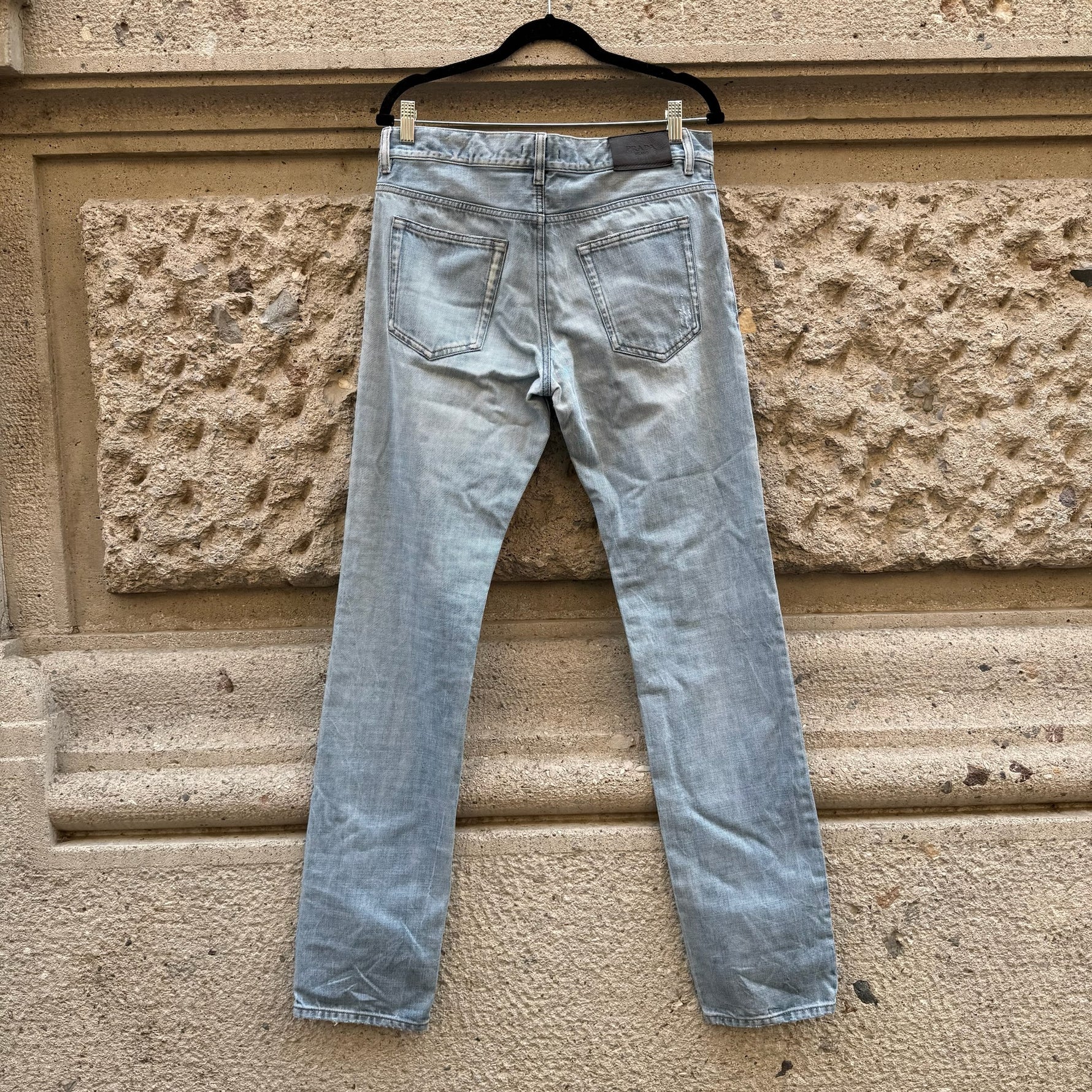 Back view of Prada light blue slim-fit jeans highlighting the minimalist back pockets, subtle fading, and signature Prada leather logo patch.