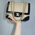 Front view of a vintage Chanel black and cream quilted flap bag featuring gold-tone CC turn-lock hardware, contrast patent leather trim, and chain shoulder straps.