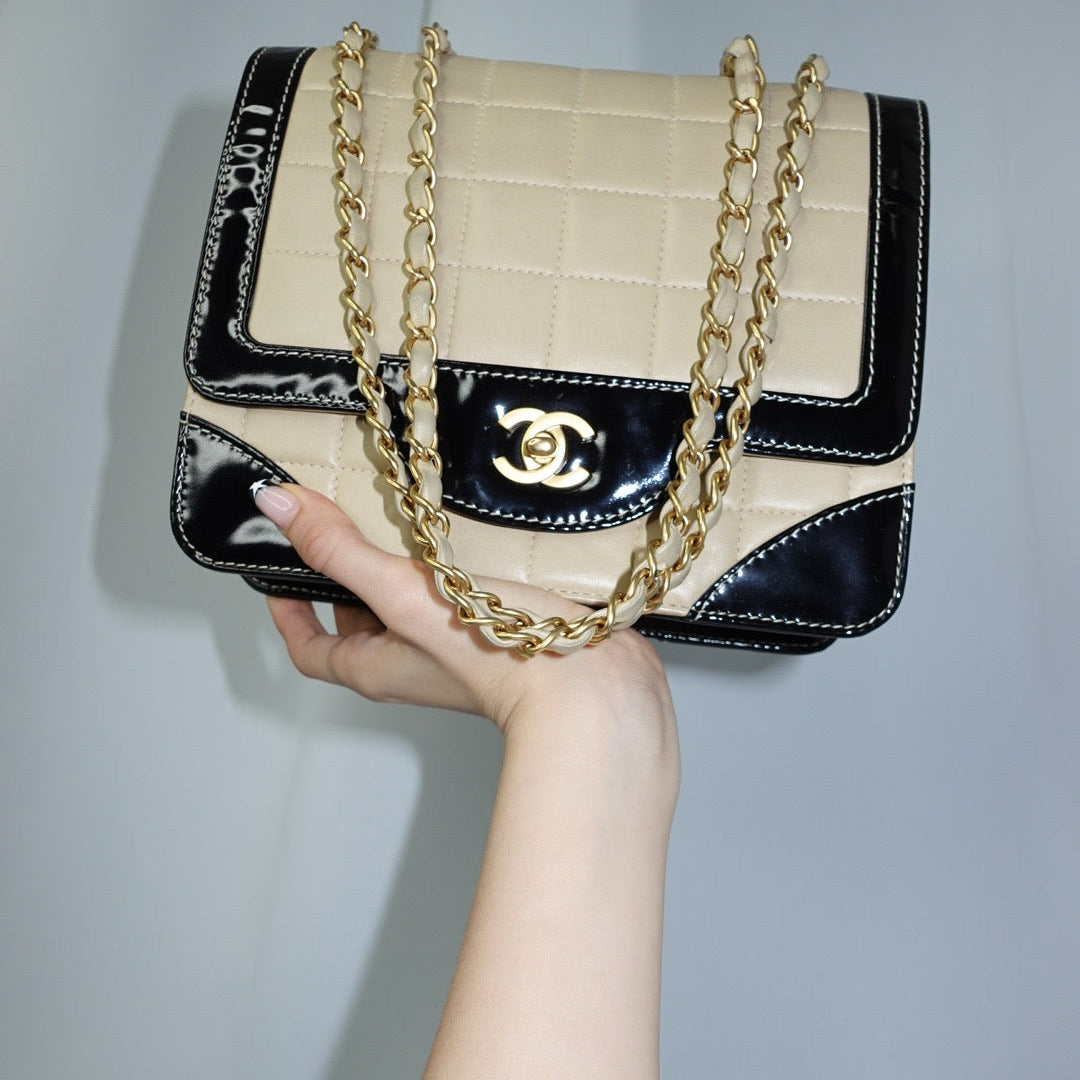 Front view of a vintage Chanel black and cream quilted flap bag featuring gold-tone CC turn-lock hardware, contrast patent leather trim, and chain shoulder straps.