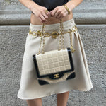 Model carrying a vintage Chanel black and cream quilted flap bag with gold-tone CC hardware, contrast patent leather accents, and chain shoulder straps.