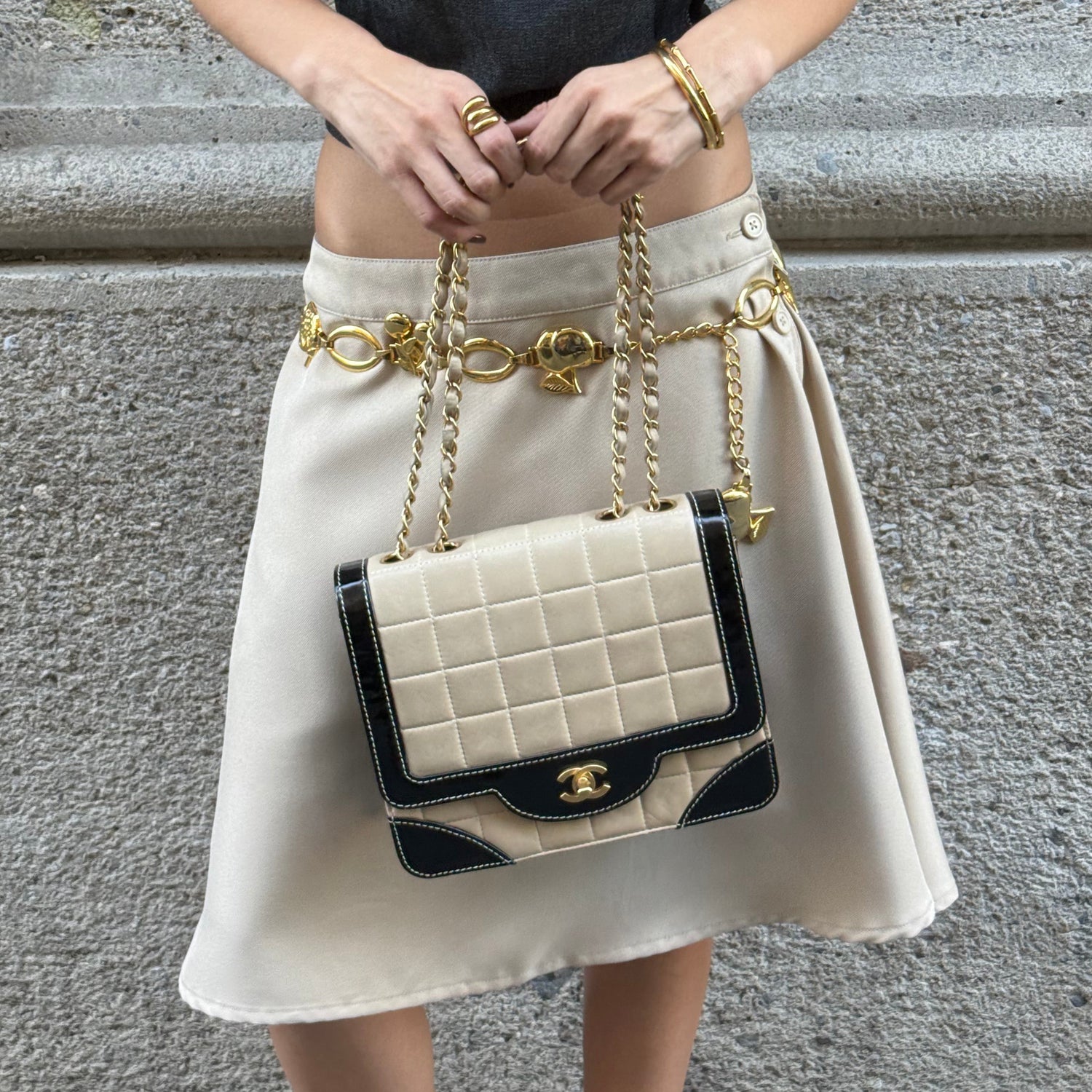 Model carrying a vintage Chanel black and cream quilted flap bag with gold-tone CC hardware, contrast patent leather accents, and chain shoulder straps.