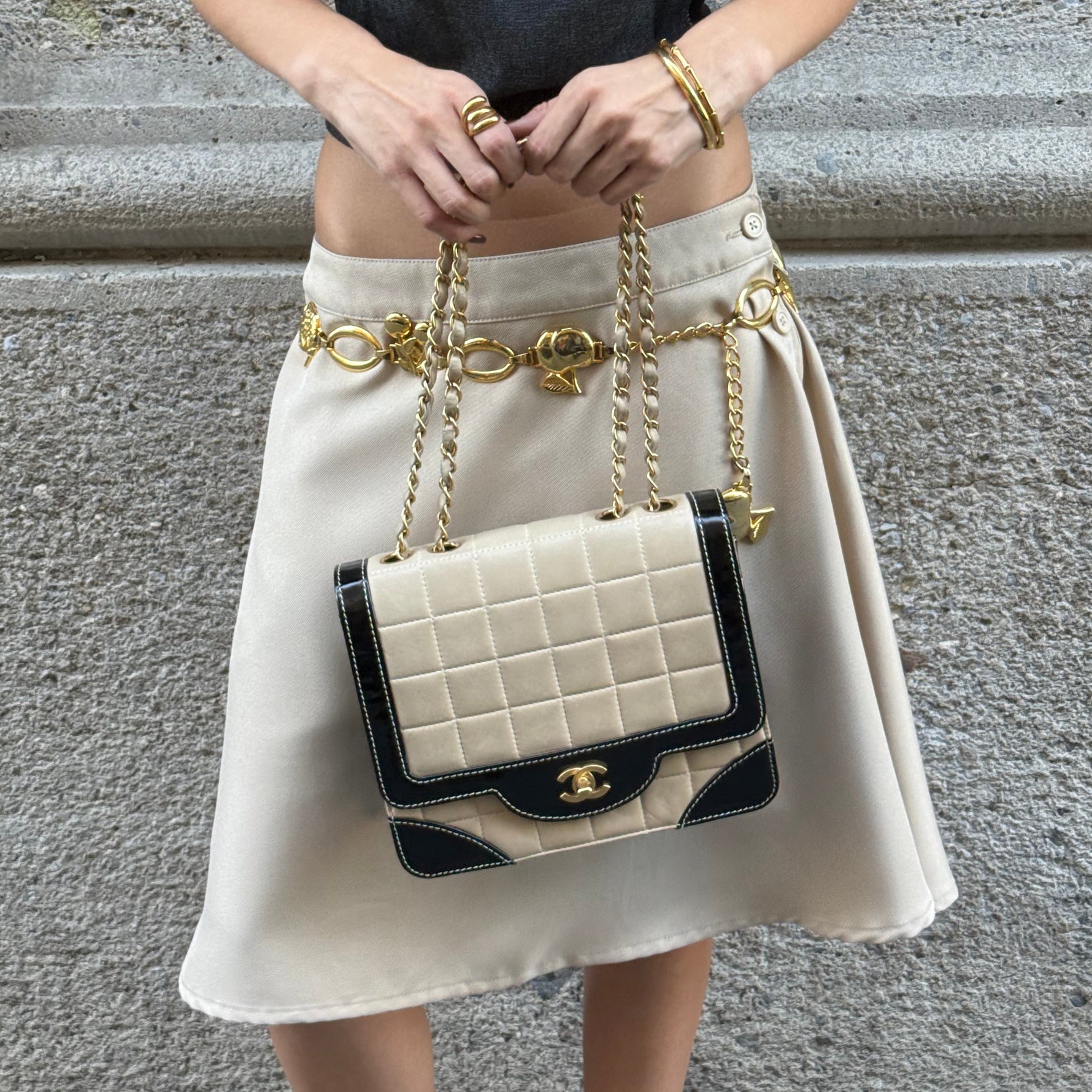 Model carrying a vintage Chanel black and cream quilted flap bag with gold-tone CC hardware, contrast patent leather accents, and chain shoulder straps.